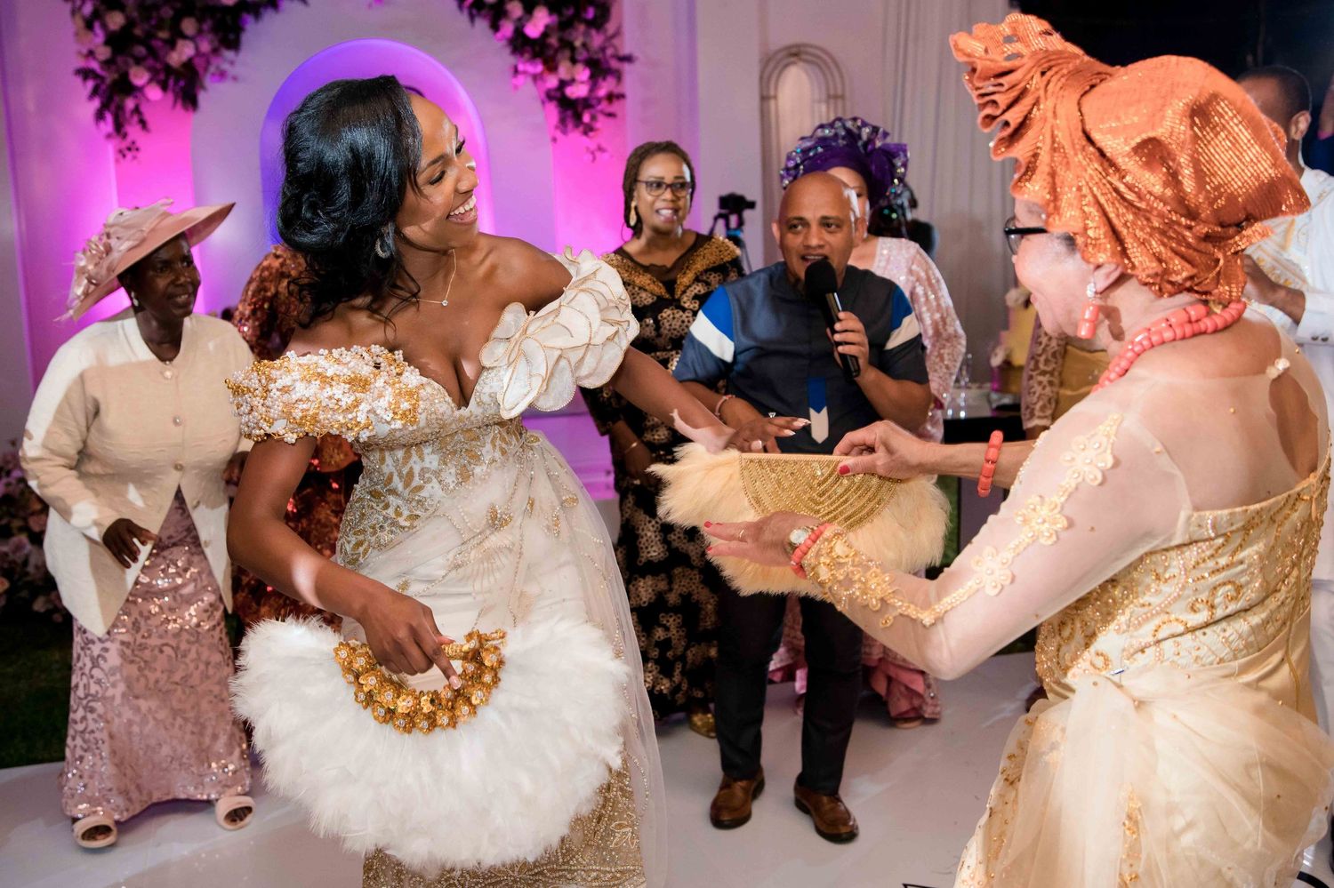 Wedding reception guests dancing and celebrating in an elegantly decorated venue with purple lighting.