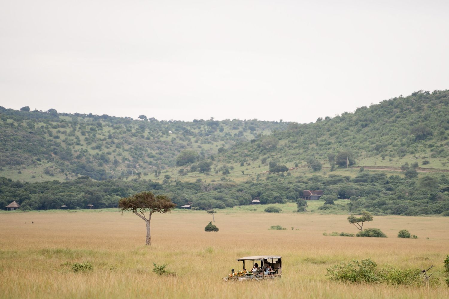 A lone safari vehicle traverses the vast African savanna landscape with scattered acacia trees.