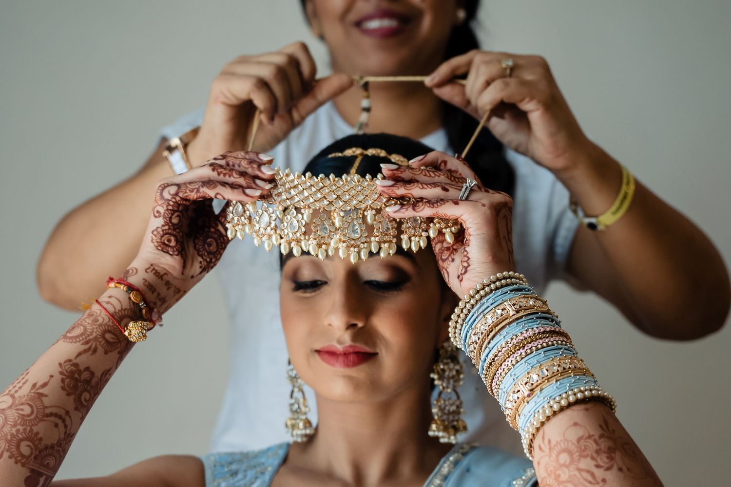 Traditional Indian bridal jewelry and headpiece being carefully placed during wedding preparation.