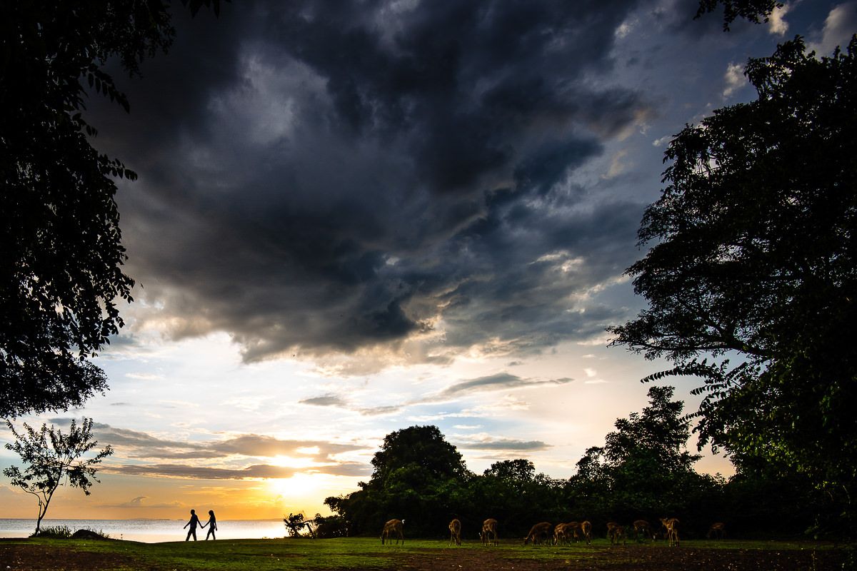 Dramatic storm clouds roll across a dark landscape with silhouetted figures on the horizon.