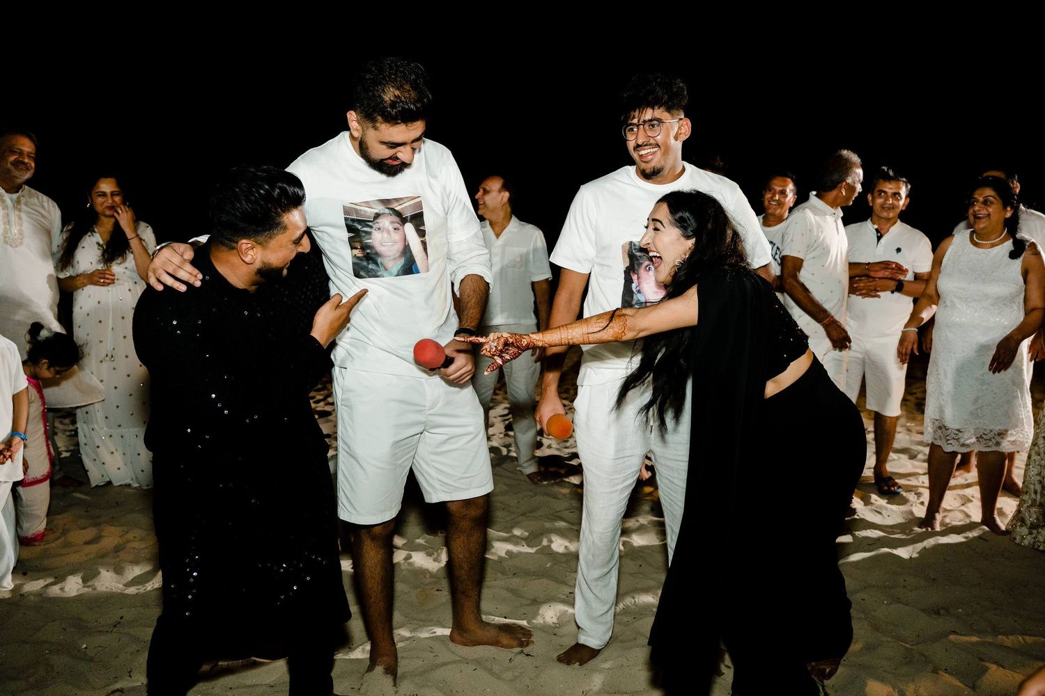 People in white and black outfits dancing and celebrating together at a nighttime beach gathering.