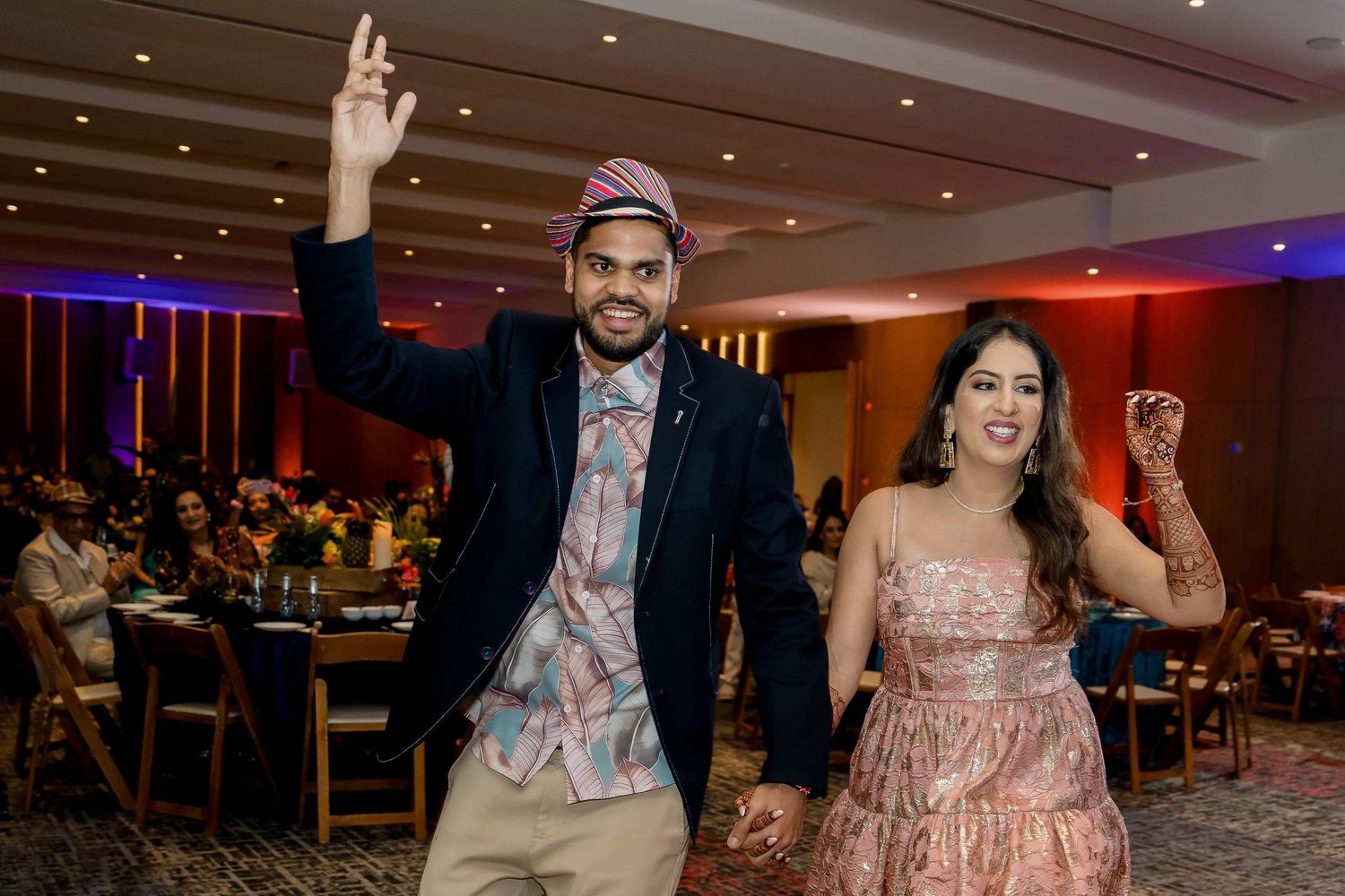 Couple makes grand entrance at wedding reception with raised hands and joyful expressions.