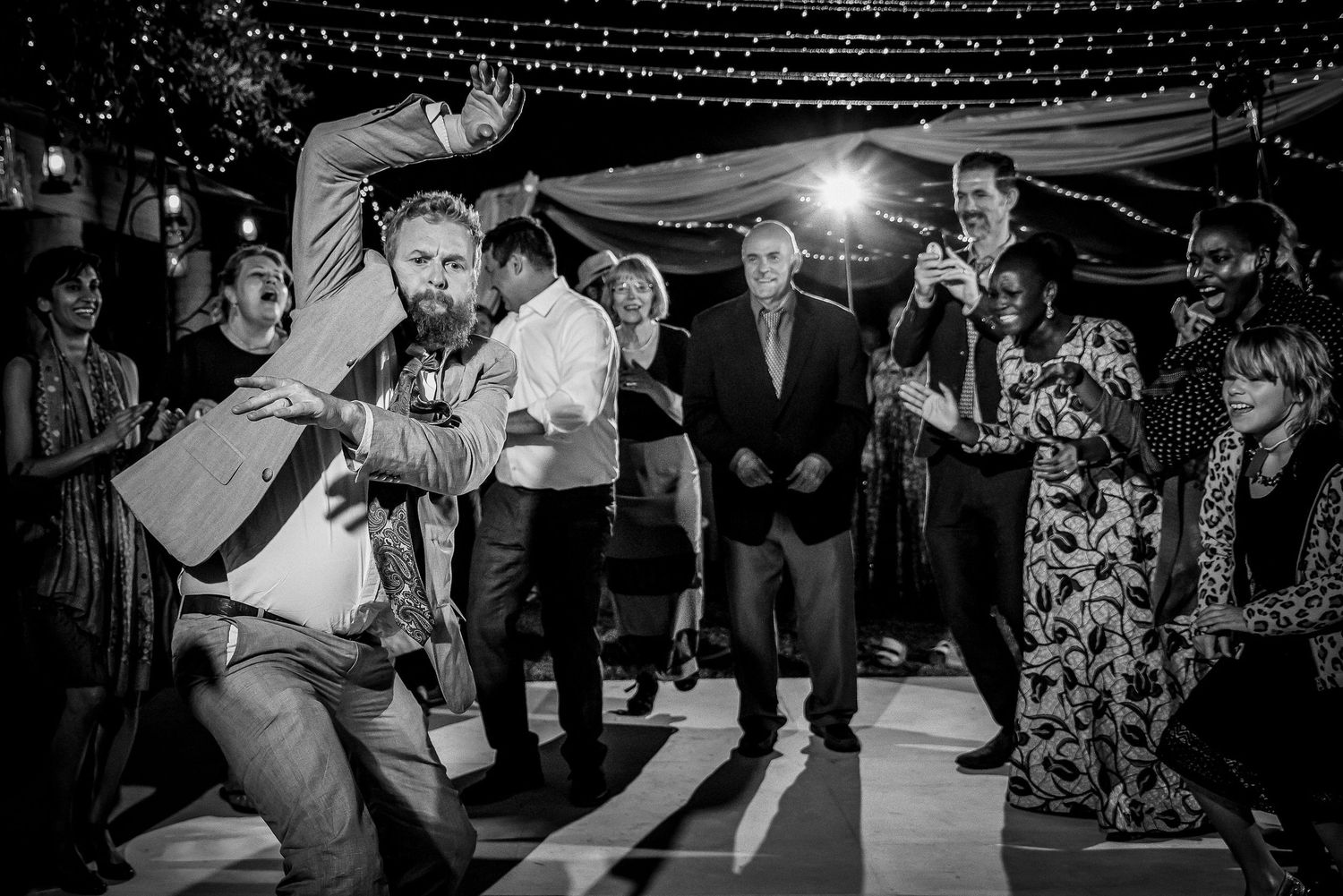 Wedding reception dance floor filled with guests celebrating under tent lighting.