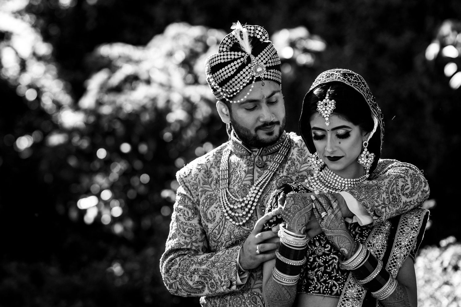 Traditional Indian wedding couple in ornate outfits shown in black and white photography.