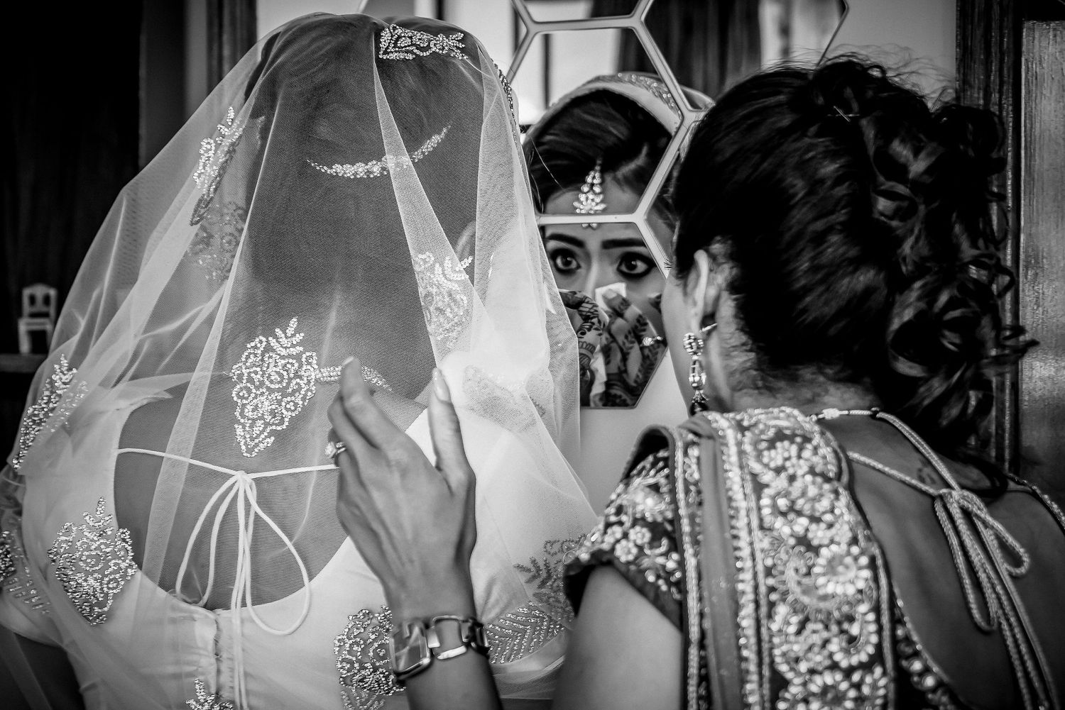 Black and white image showing intricate details of a bride's lace wedding dress being adjusted.