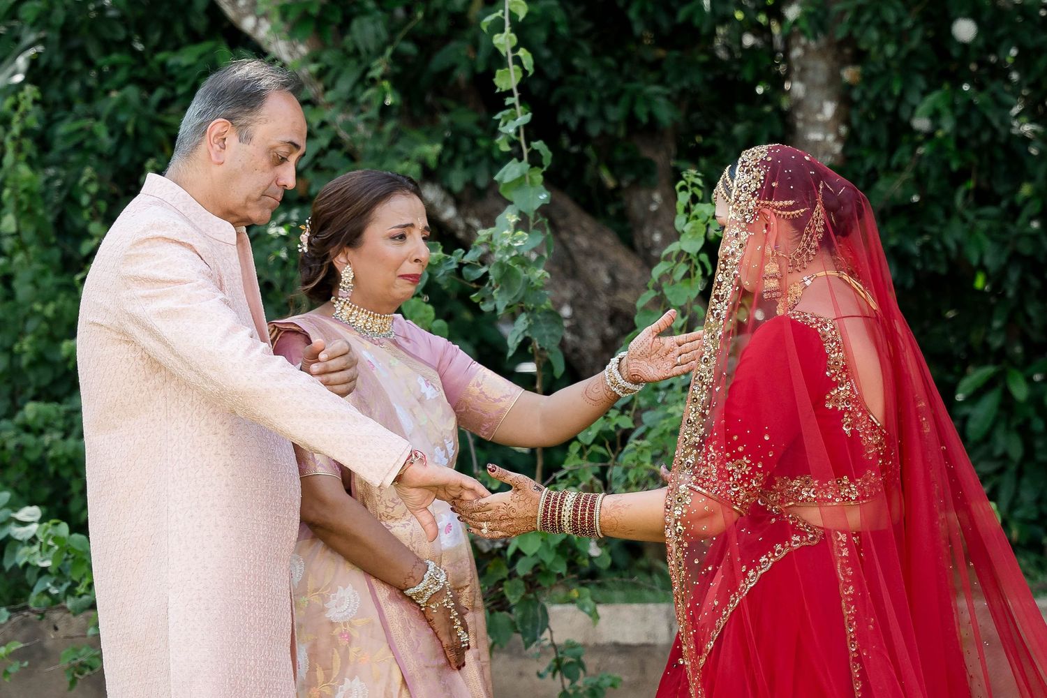 Traditional Indian wedding ceremony featuring couples in red and gold attire exchanging garlands in an outdoor garden setting.