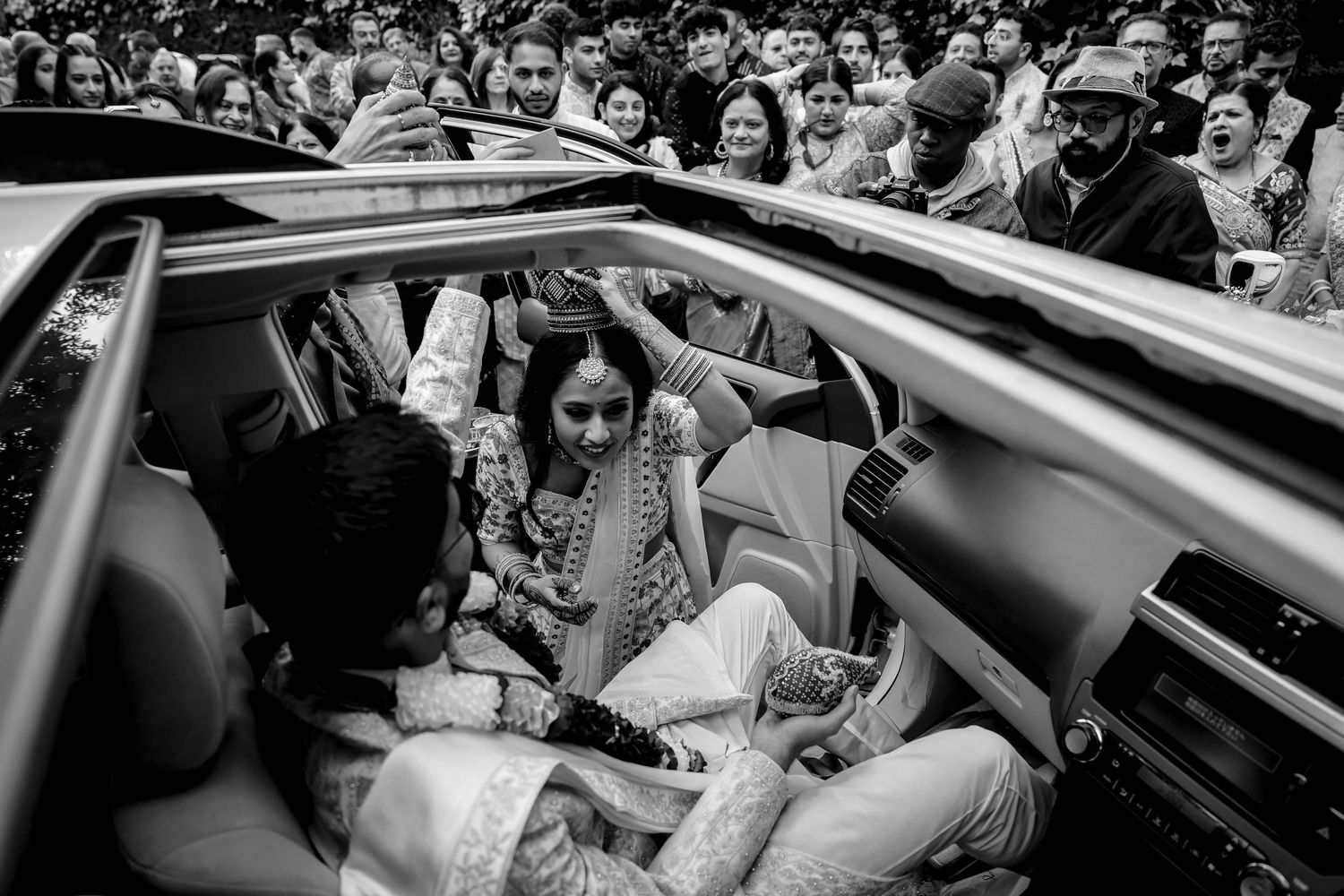 Black and white photograph capturing an intimate moment during a wedding ceremony inside a car.