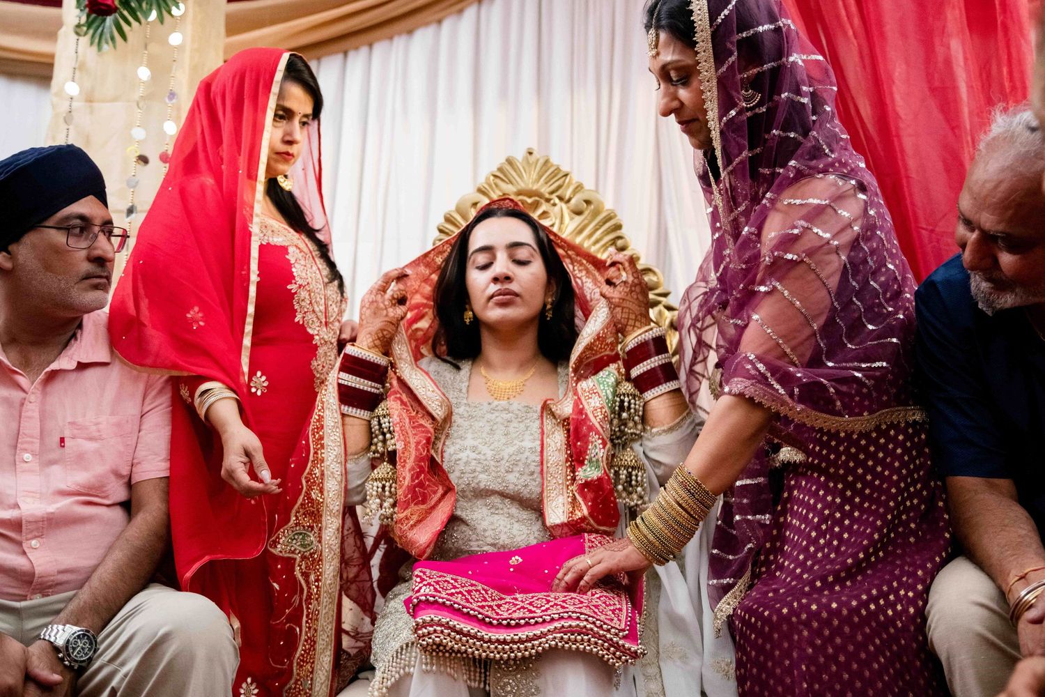 Traditional Indian bride seated on ornate chair during wedding ceremony preparations.