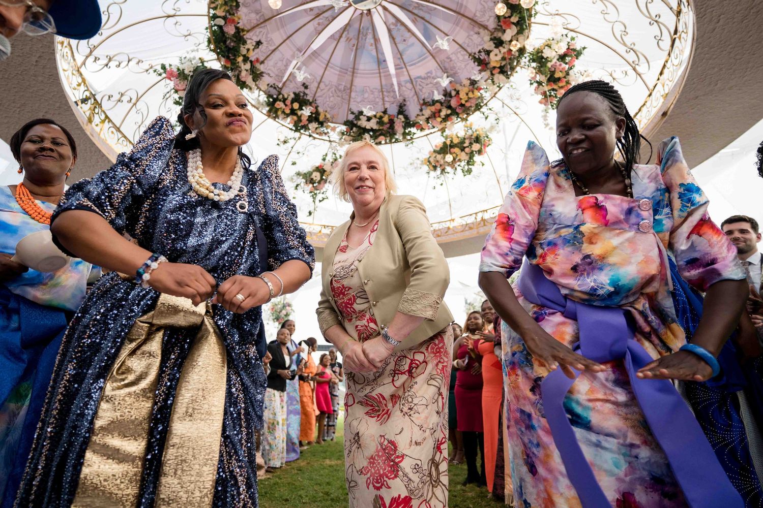 Wedding guests dance and celebrate under decorative pink paper parasols at an outdoor reception.