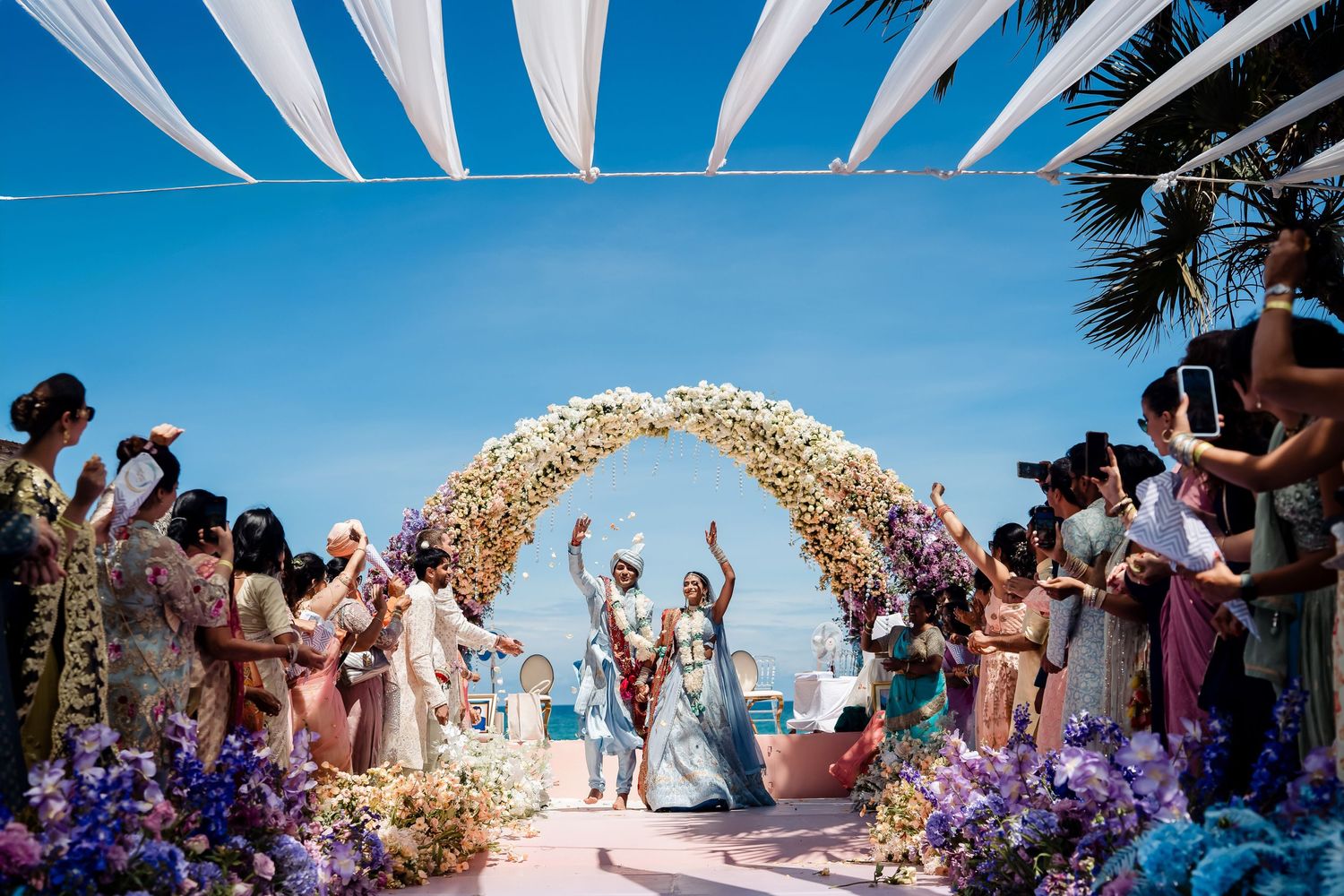 Joyous celebration under floral arch at beachside wedding ceremony.