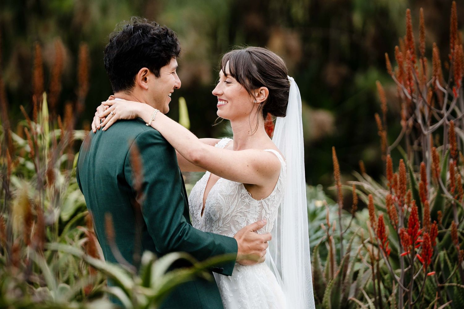 A romantic moment captured between newlyweds surrounded by natural foliage and red flowering plants.