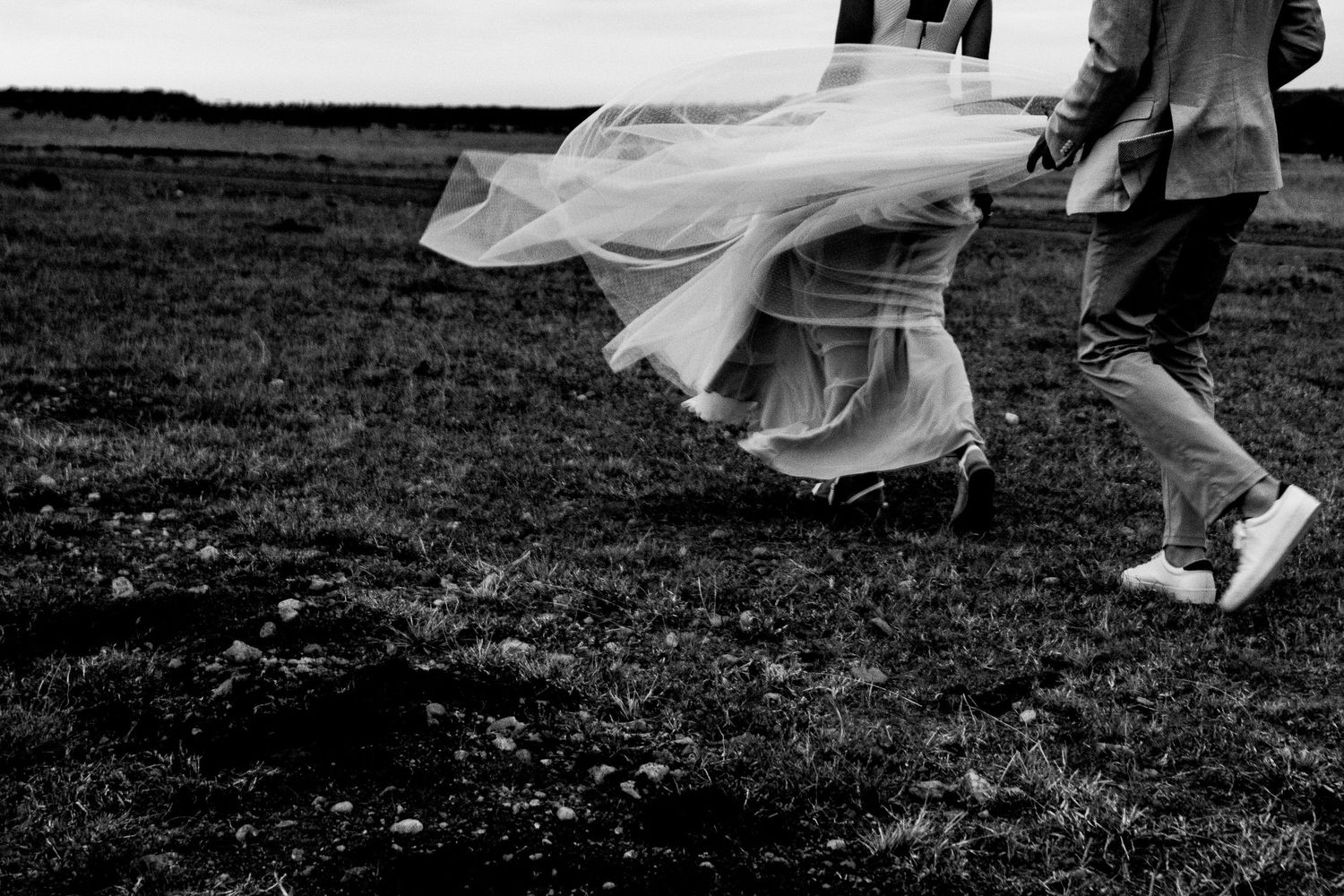Flowing white dress catches wind as couple walks across hillside in black and white.