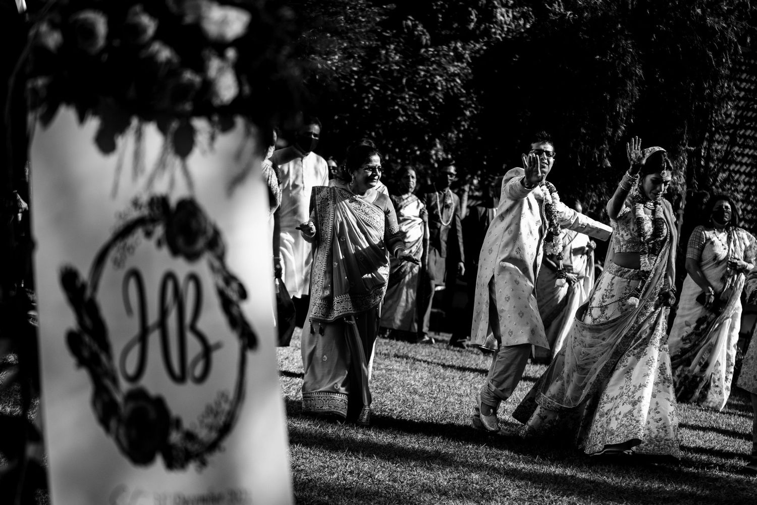 Black and white wedding party processional walking outdoors with decorative lighting.