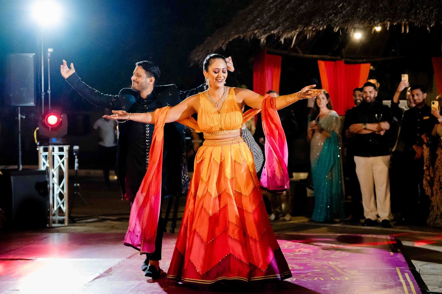 Dramatic nighttime dance floor scene with colorful lighting and dancing silhouettes at a wedding celebration.