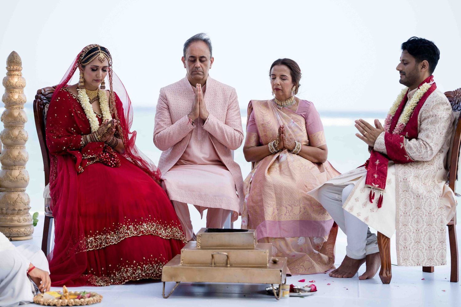 Traditional Indian wedding ceremony guests seated in rows with hands clasped in prayer during ritual.