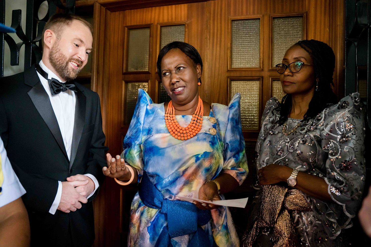 Three people engaged in lively conversation at a formal event, with one wearing a vibrant blue dress and orange necklace.