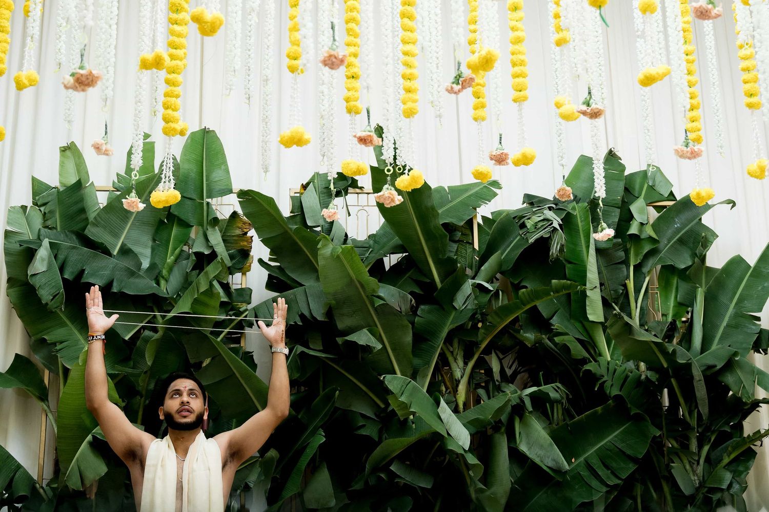 Celebrant raises hands against backdrop of tropical leaves and yellow string decorations.