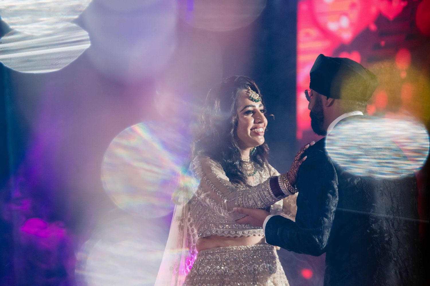 A couple shares a joyful moment on the dance floor with colorful bokeh lighting effects.