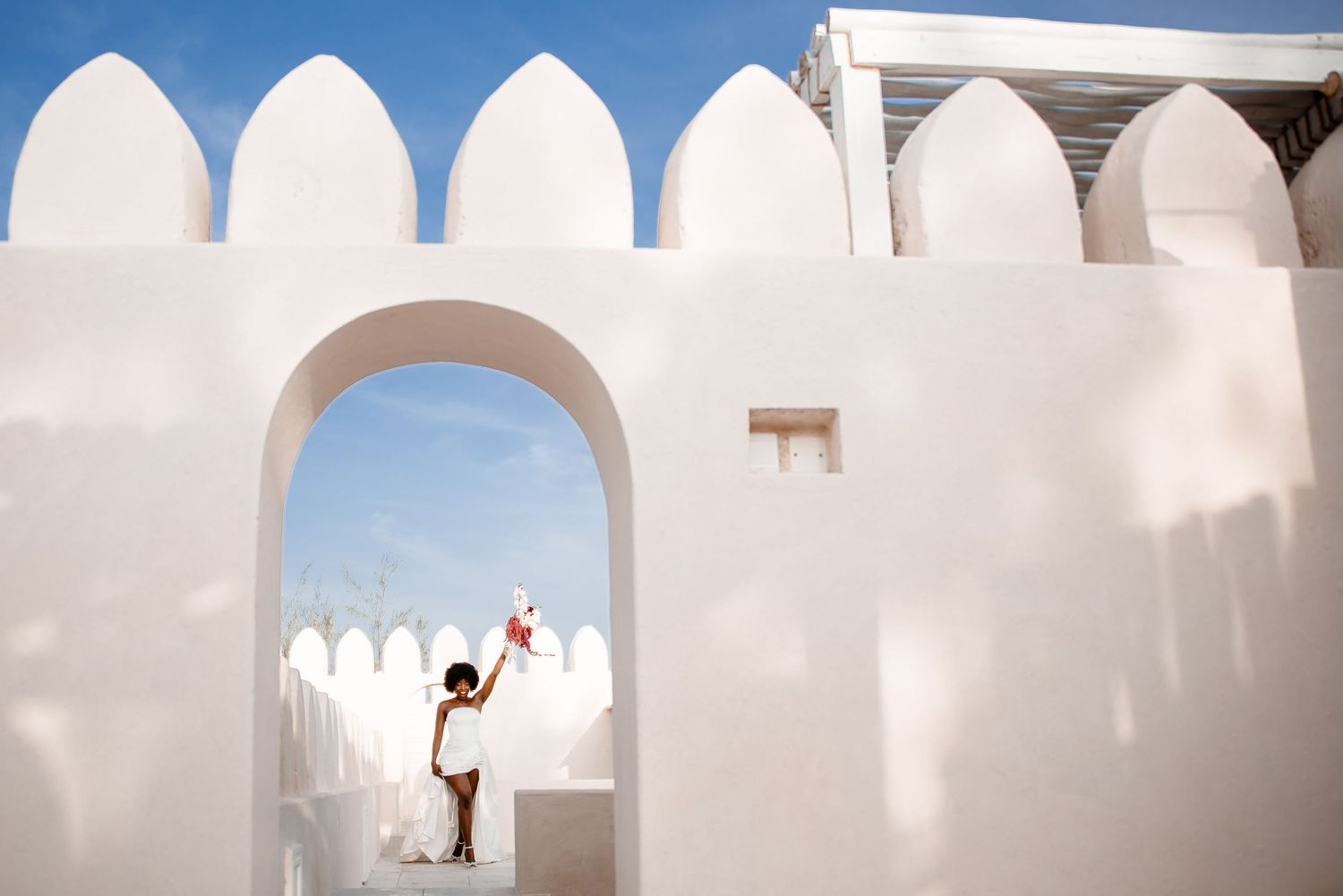 A series of white arched doorways and columns create a minimalist architectural pattern against a blue sky.