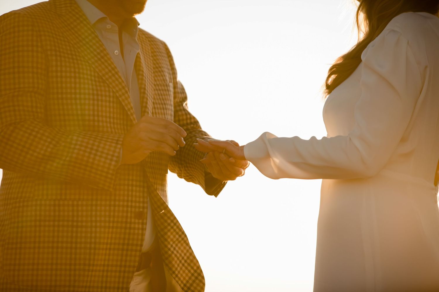 Couple exchanging rings during an outdoor ceremony with sunlight streaming through.