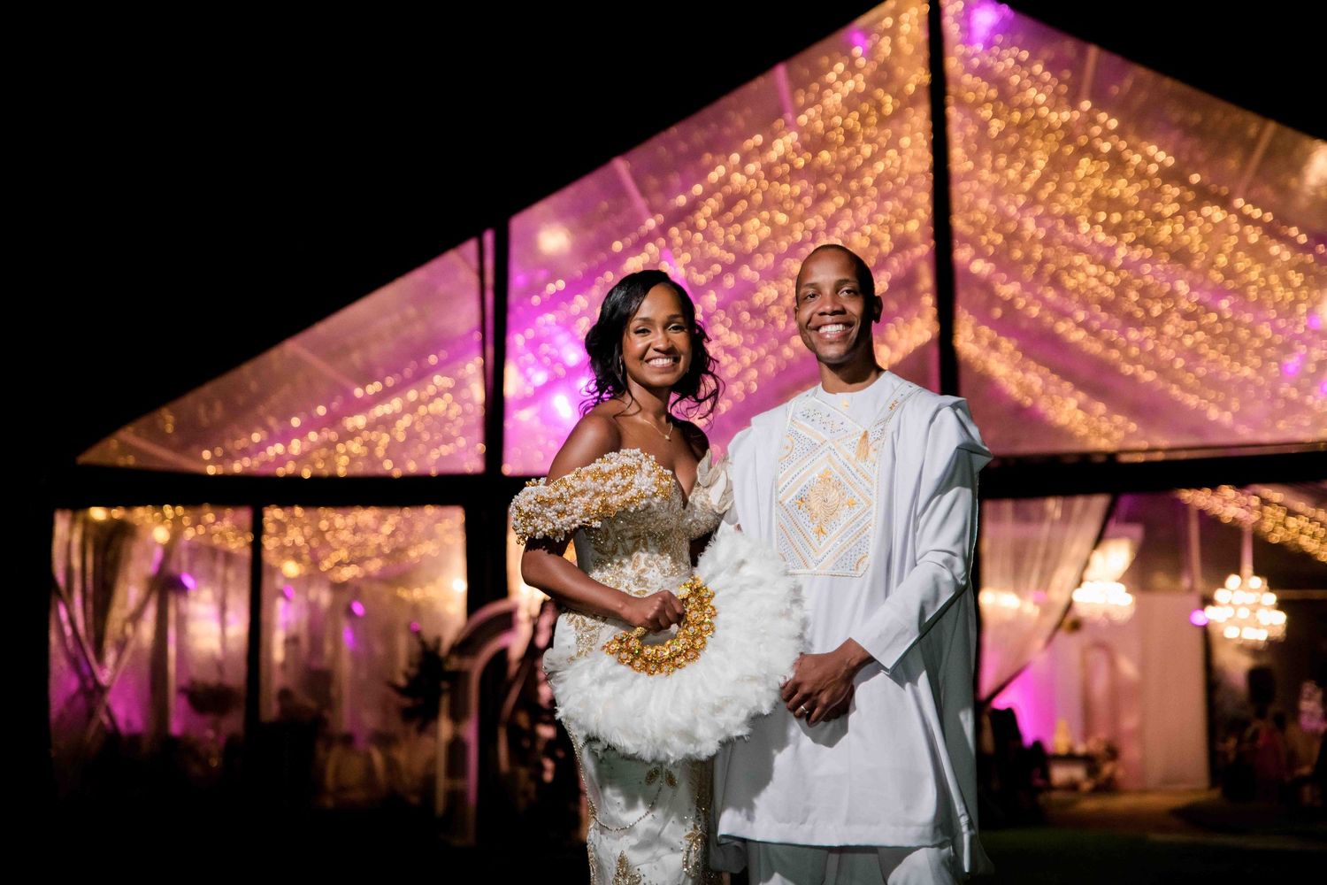 Couple poses under twinkling lights in elegant wedding reception tent.
