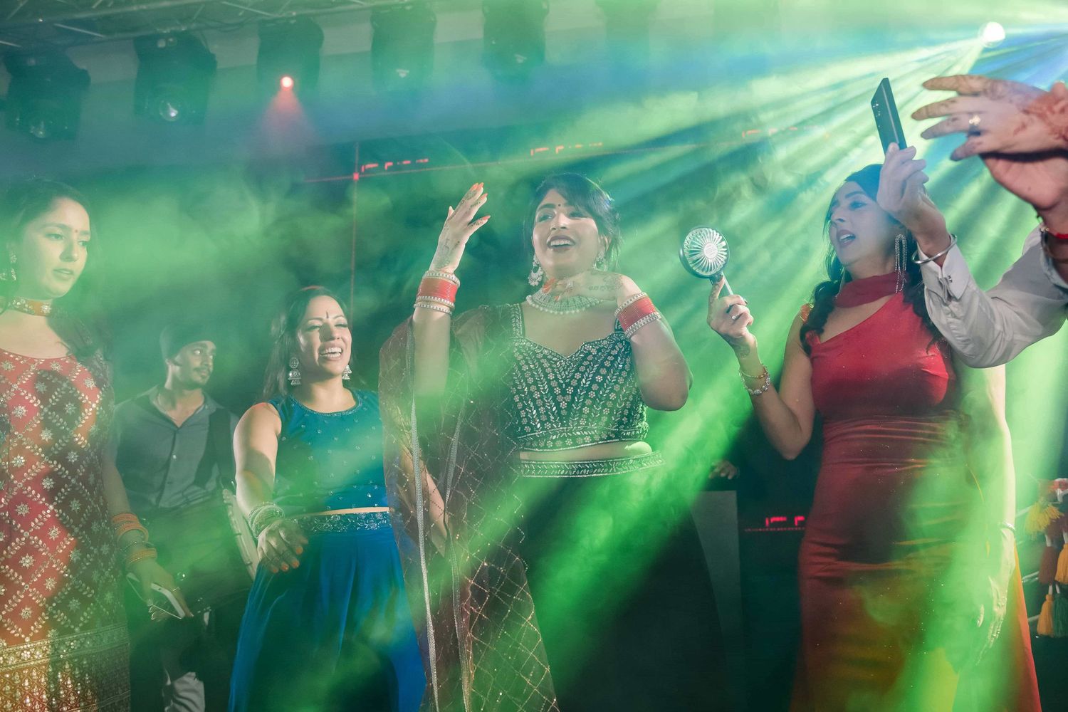 Celebratory scene with people dancing under vibrant green stage lighting.