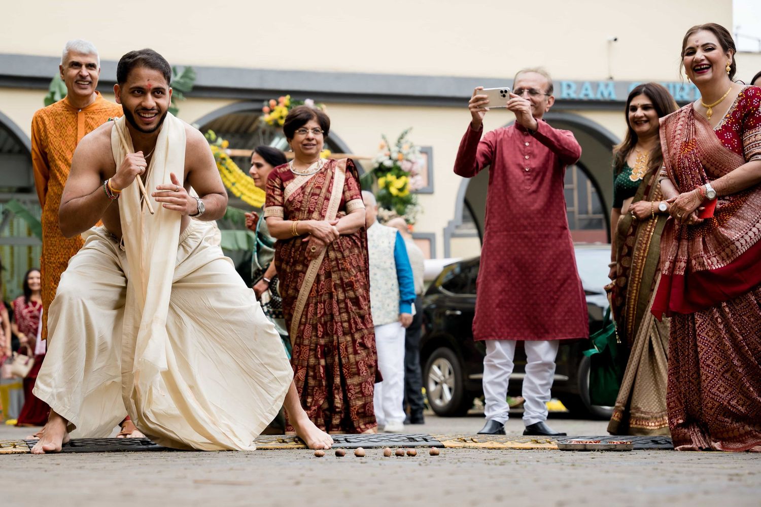Wedding guests in traditional Indian attire dancing energetically on stone pavement.