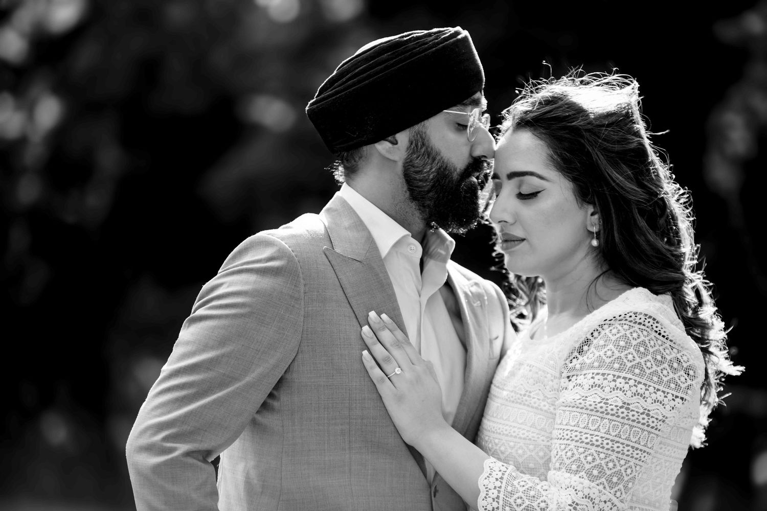 A romantic black and white portrait of a couple in a tender moment outdoors with backlighting.
