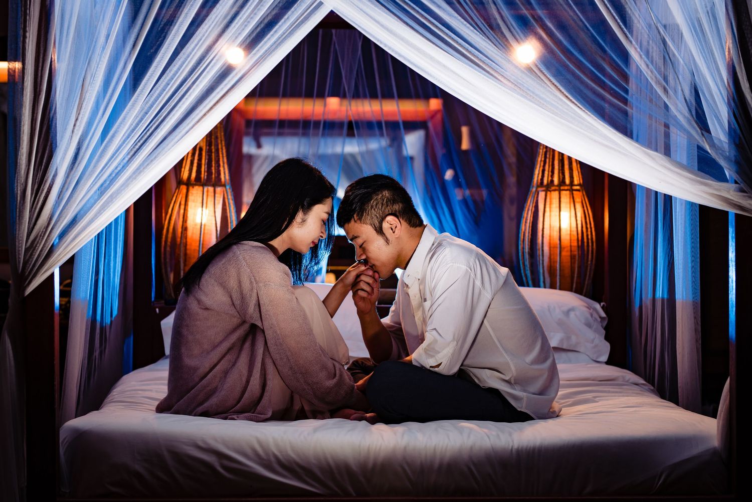 Romantic couple embraces under flowing white fabric drapes in dramatic lighting.