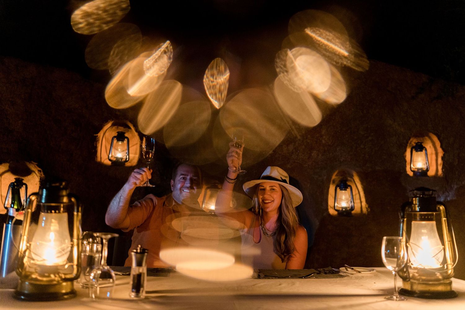 Oil lanterns illuminate an outdoor evening gathering in a safari setting.