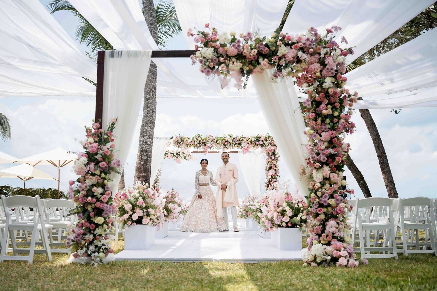 A beachside wedding ceremony setup with white chairs and pink floral arch decorations overlooking the ocean.
