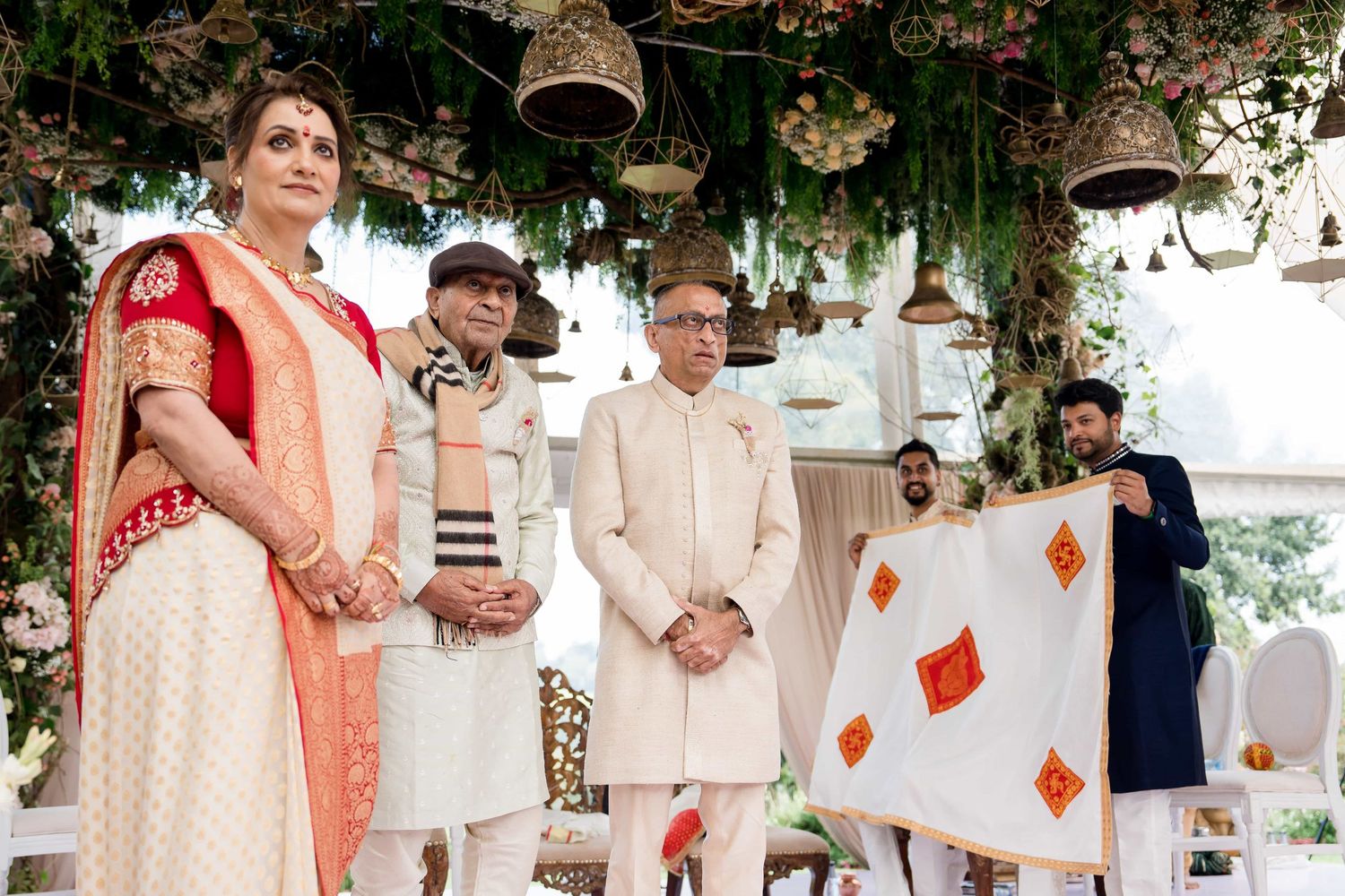 Wedding ceremony participants standing beneath decorative bells and floral arrangements.
