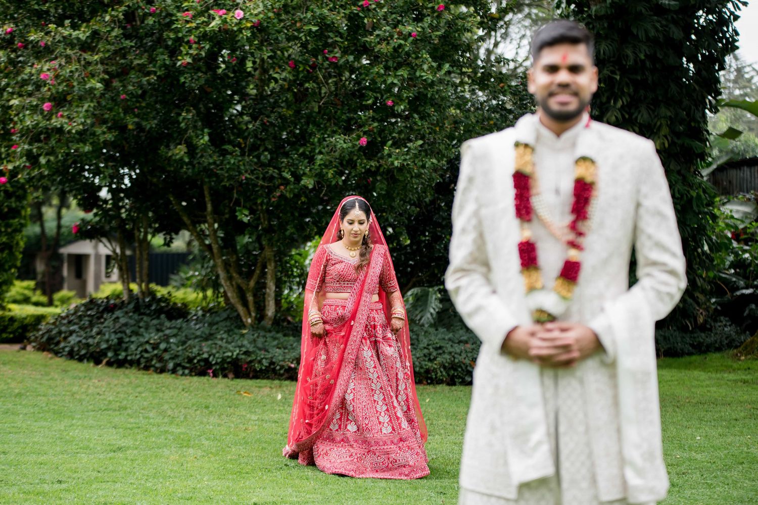 Traditional Indian wedding couple in formal attire posed in a garden setting.