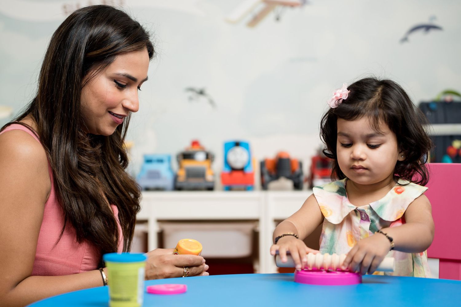 Adult and child play together with colorful toys at a blue table during indoor playtime activity.