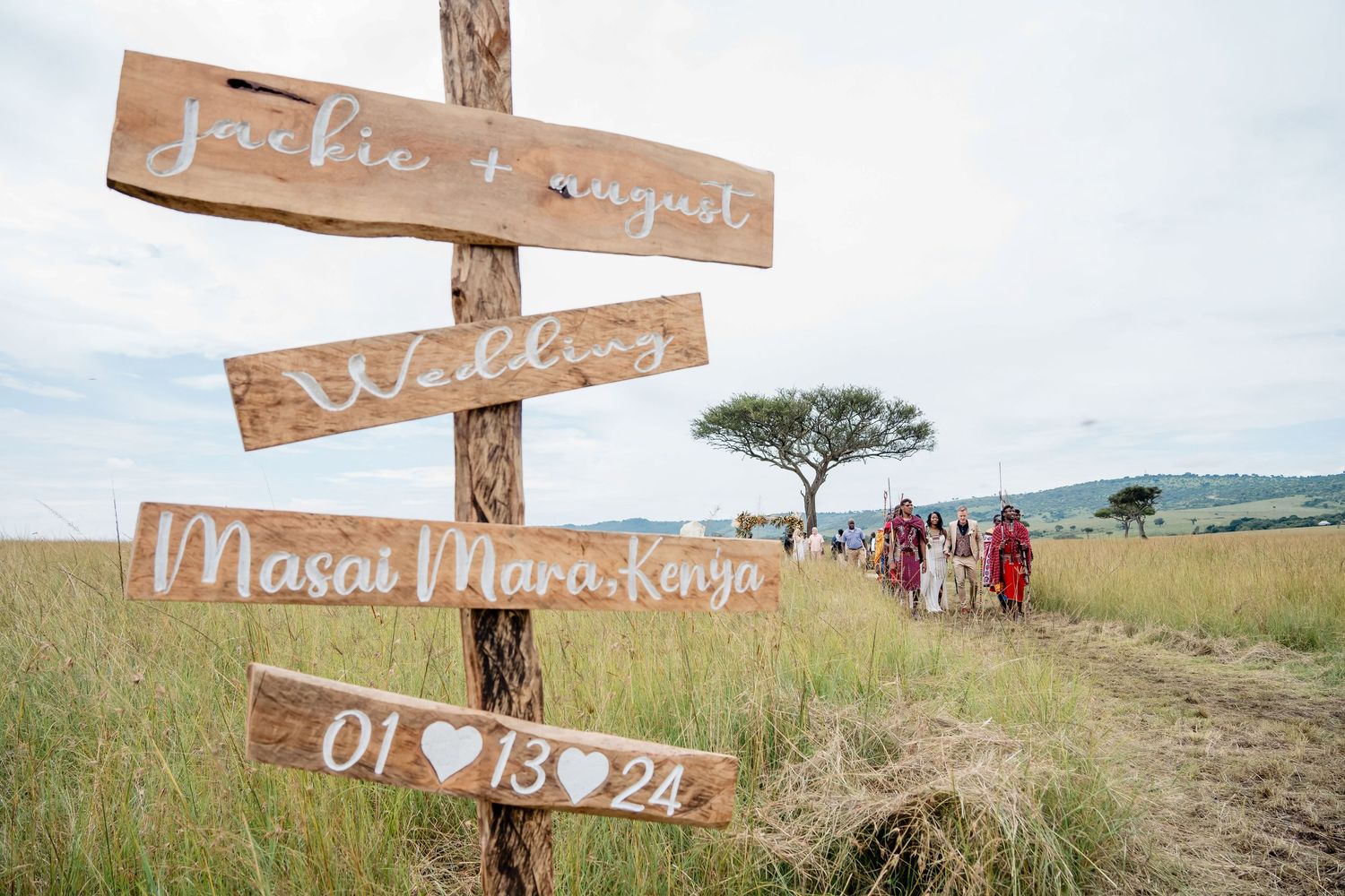 Wooden wedding sign marking location as Masai Mara, Kenya with acacia tree in background.