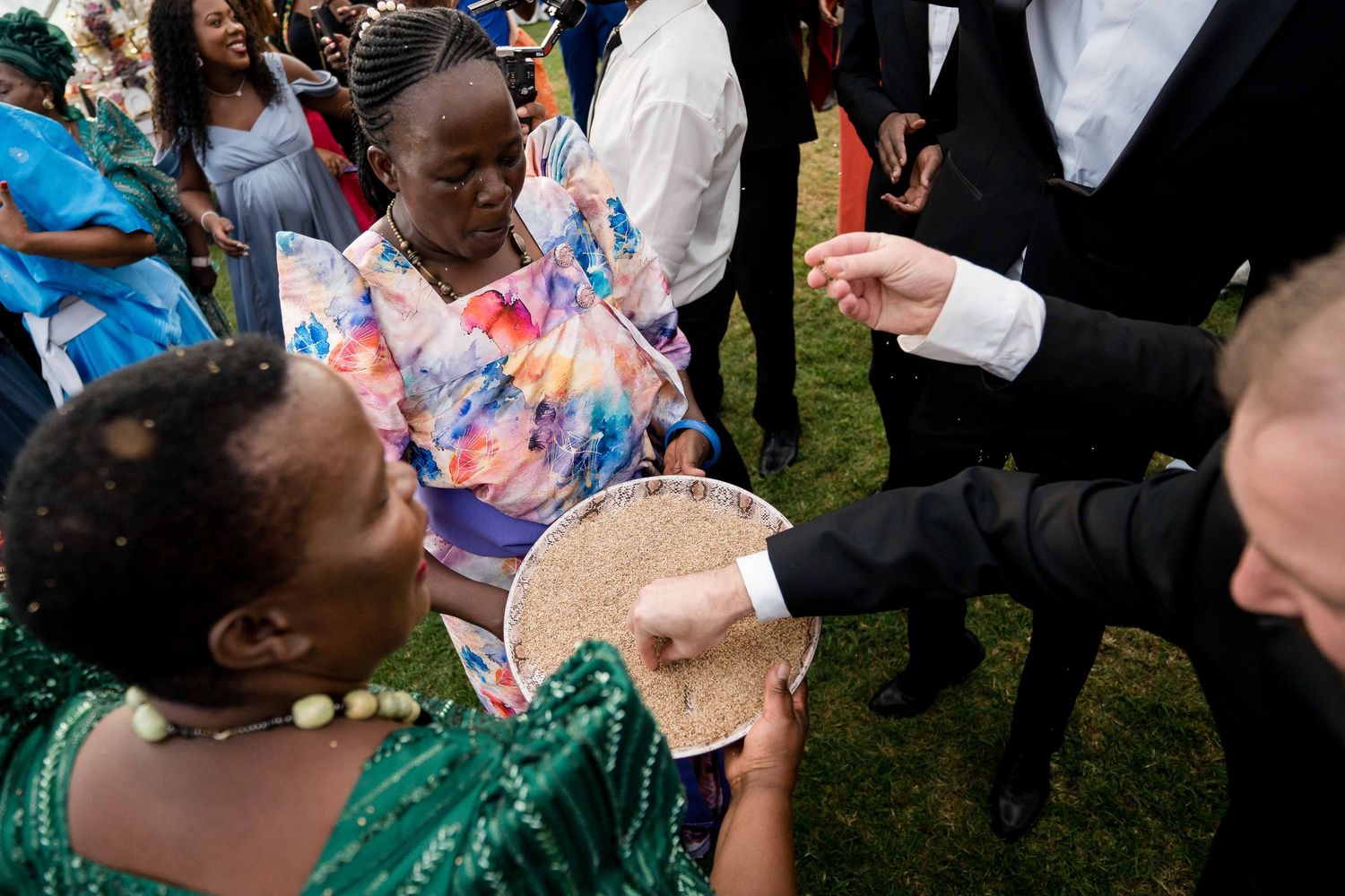 Wedding party members in formal wear interact and celebrate on a grassy lawn during an outdoor reception.