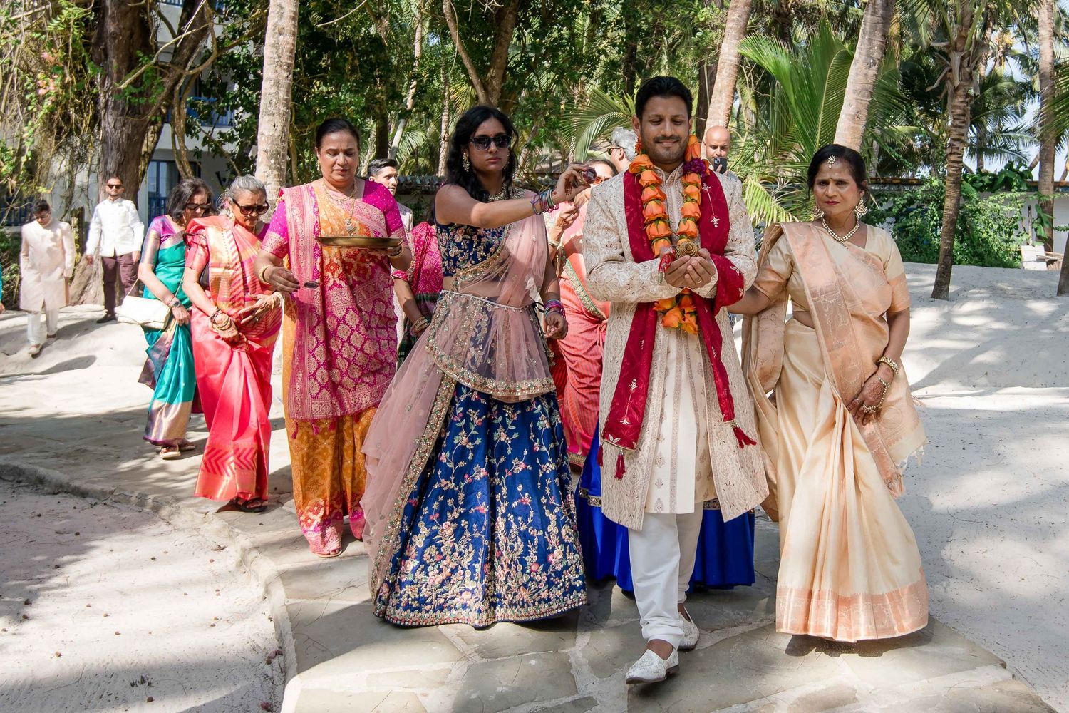 A group in traditional Indian wedding attire walking together on a tree-lined path during a celebration.