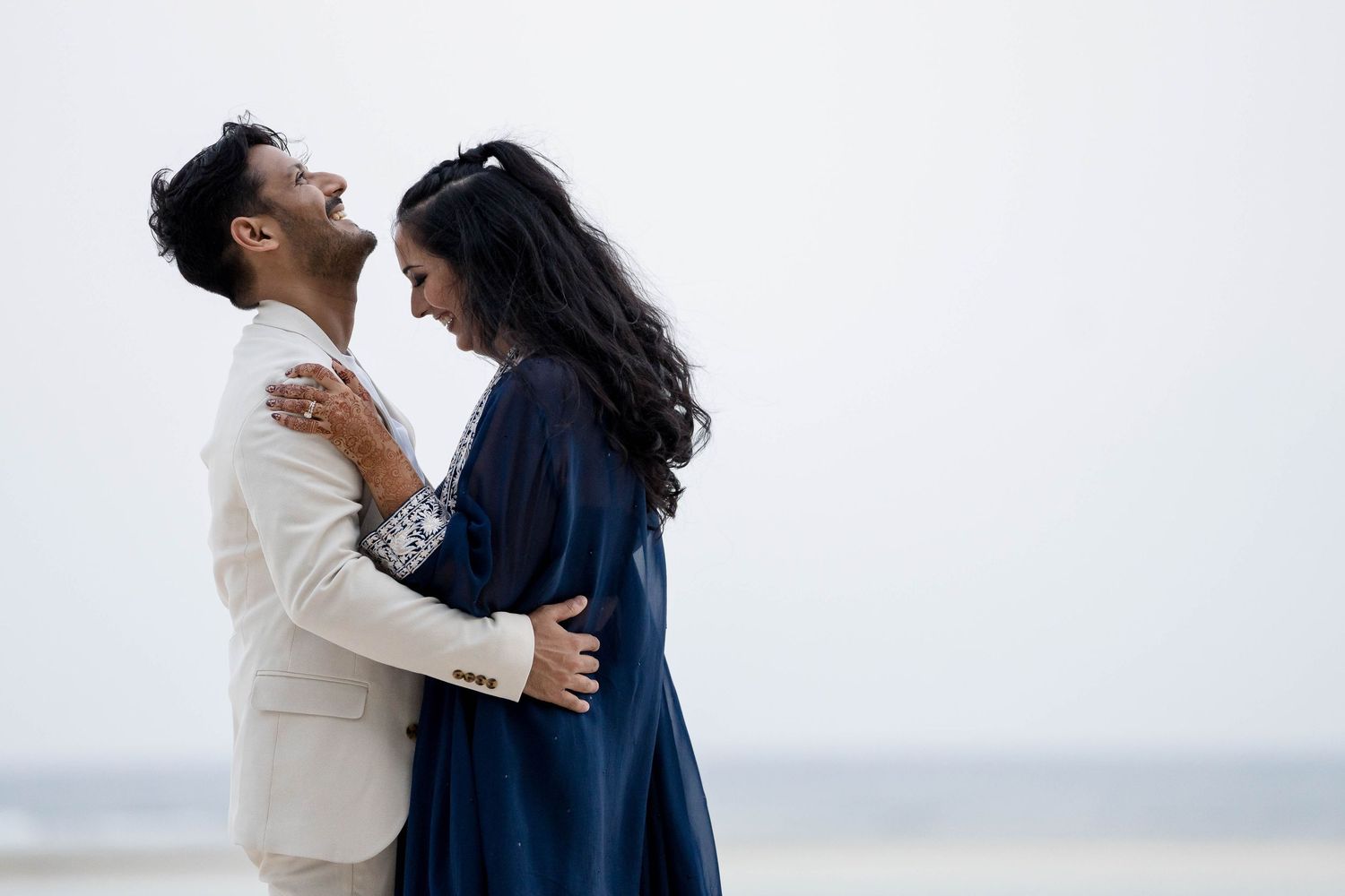 A couple in contrasting white and navy outfits embrace lovingly on a misty beach.