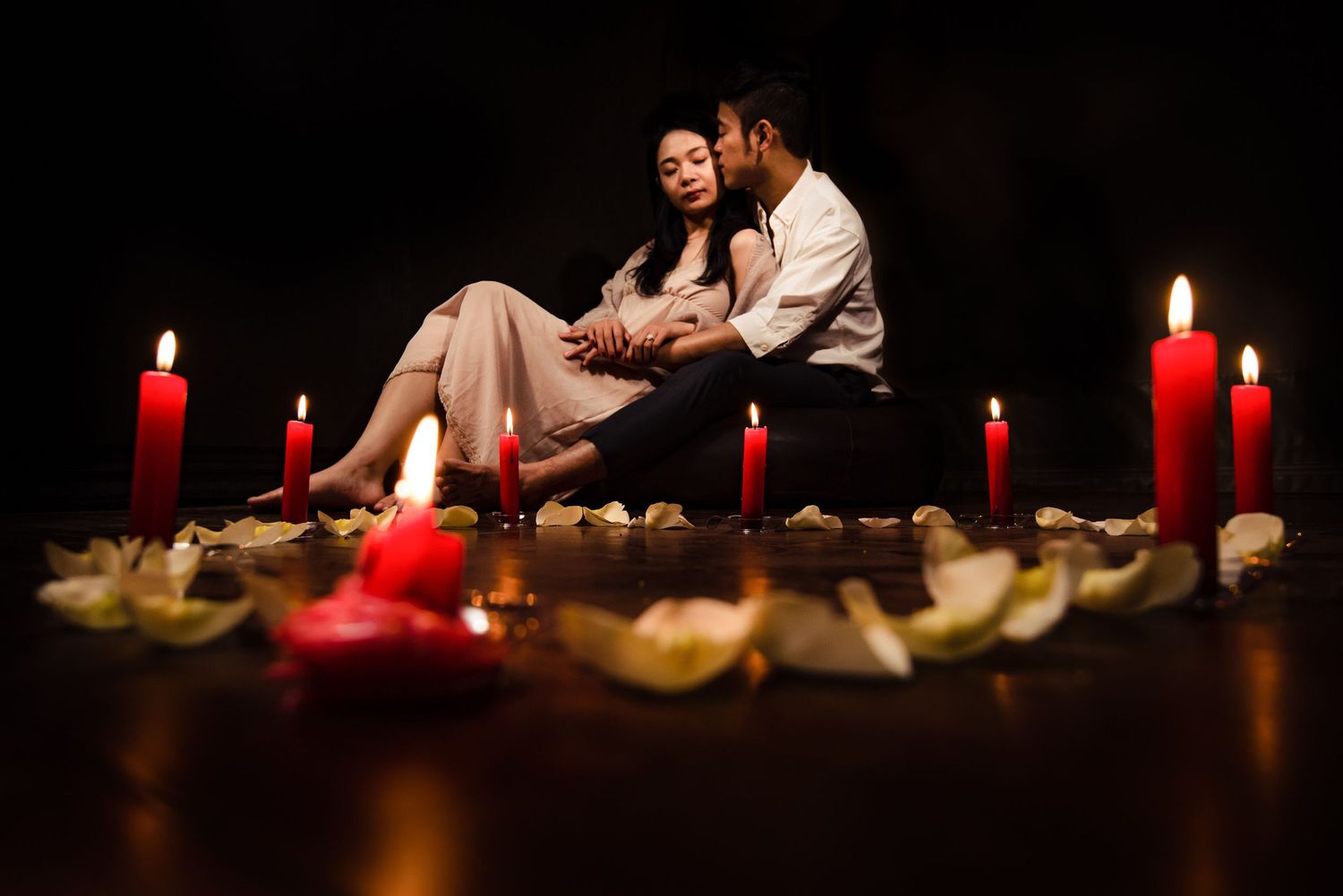 Red candles illuminate rose petals scattered on dark surface creating romantic ambiance.