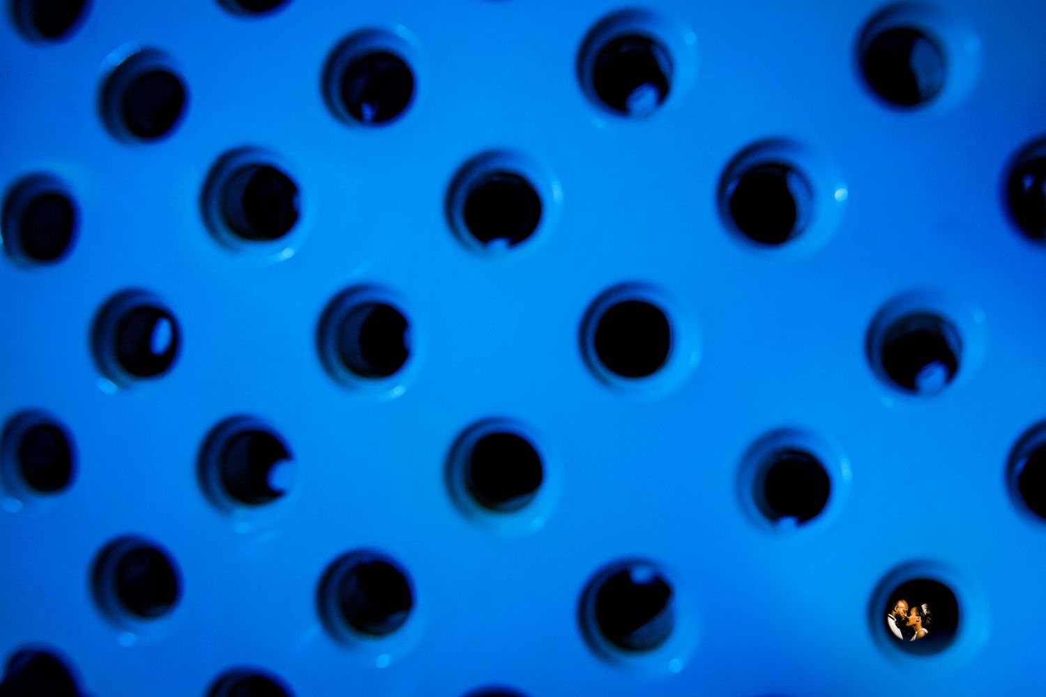 Abstract pattern of circular holes in bright blue metal surface.