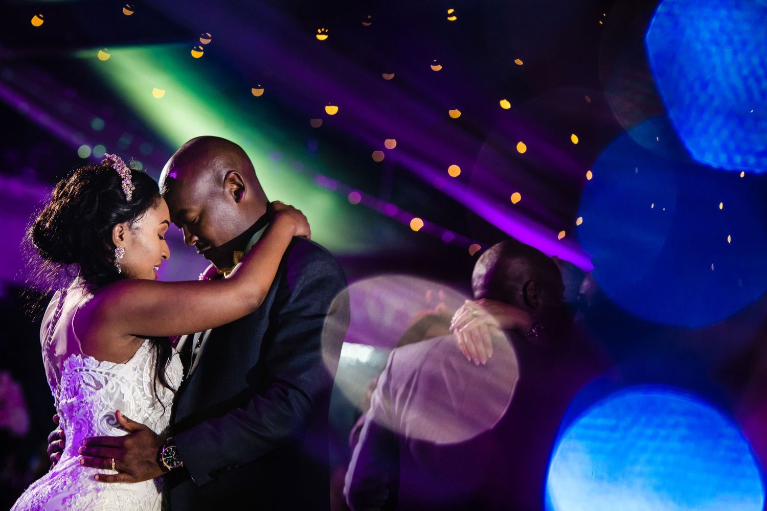 Dance couples twirl under blue and purple lighting at an elegant evening celebration.