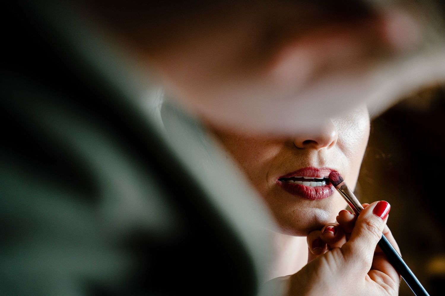 A close-up macro shot shows someone applying red lipstick in dramatic lighting.