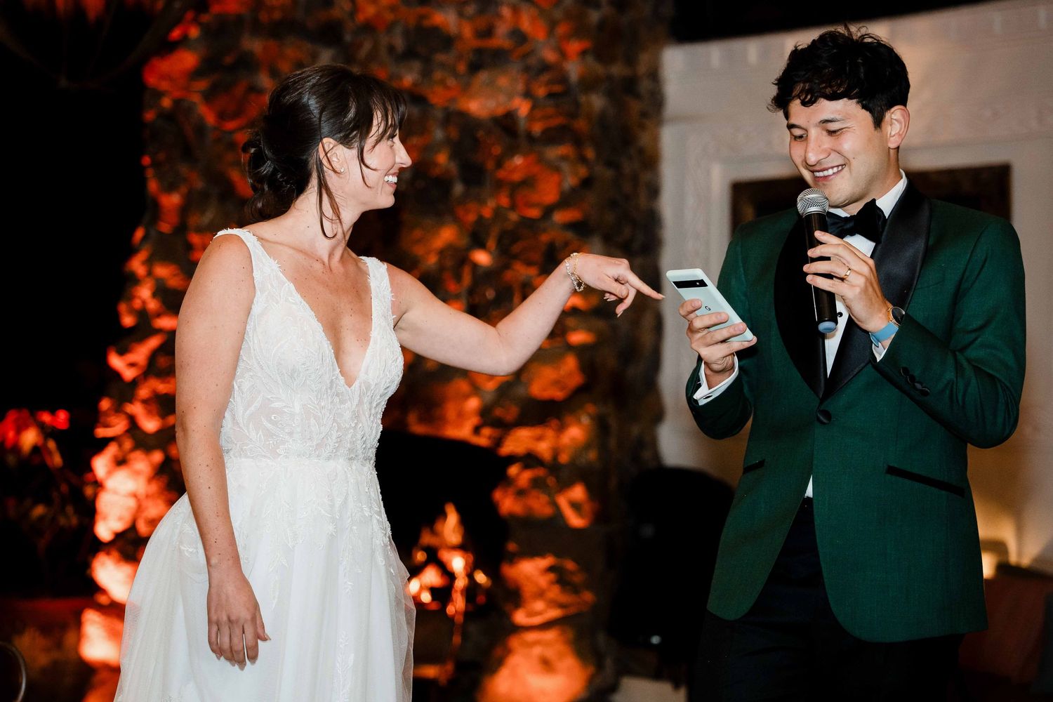 Wedding couple shares a candid moment while checking their phones during an evening reception with warm lighting.