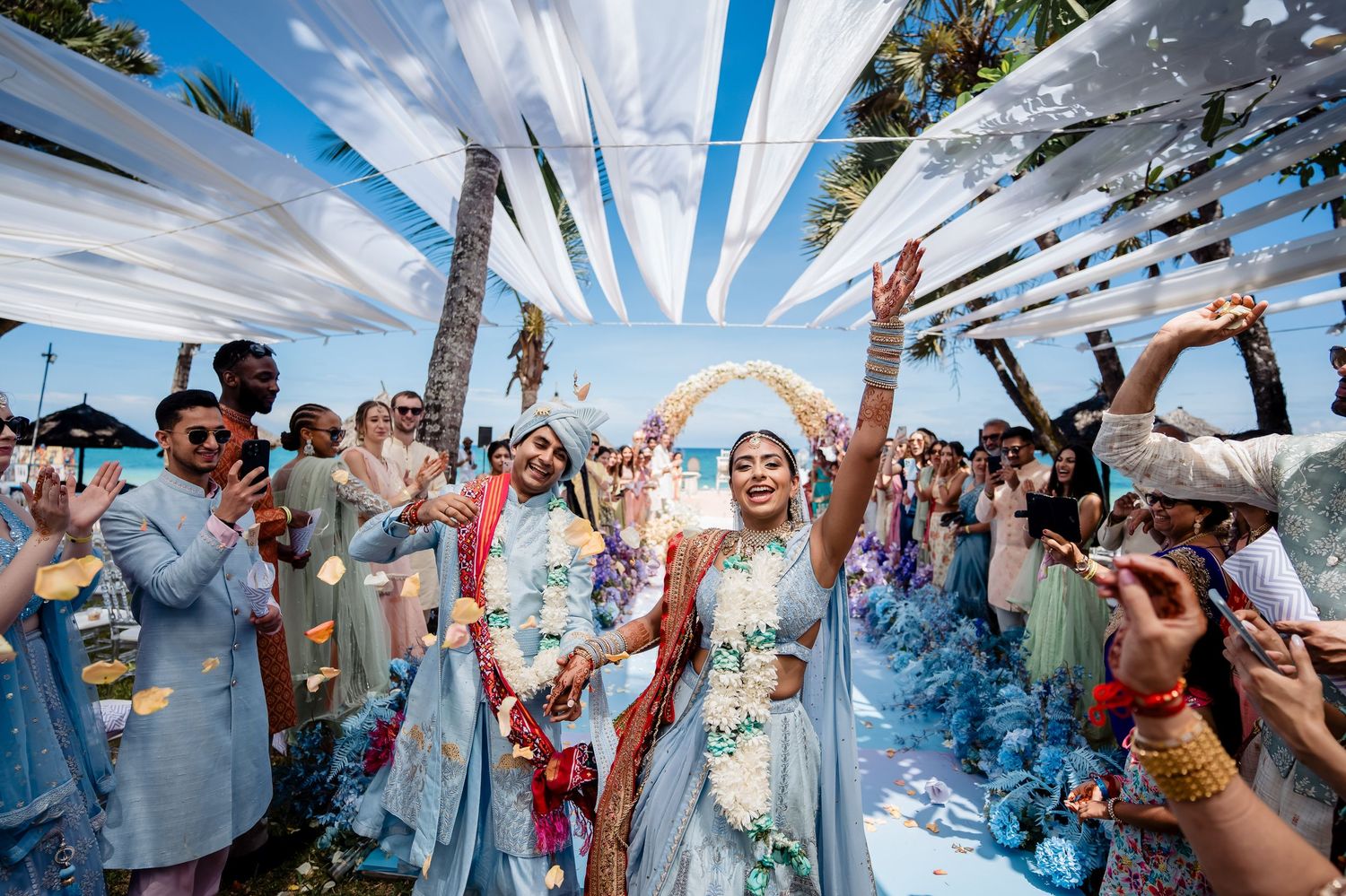 Wedding celebration with white fabric decor and confetti under bright blue sky.