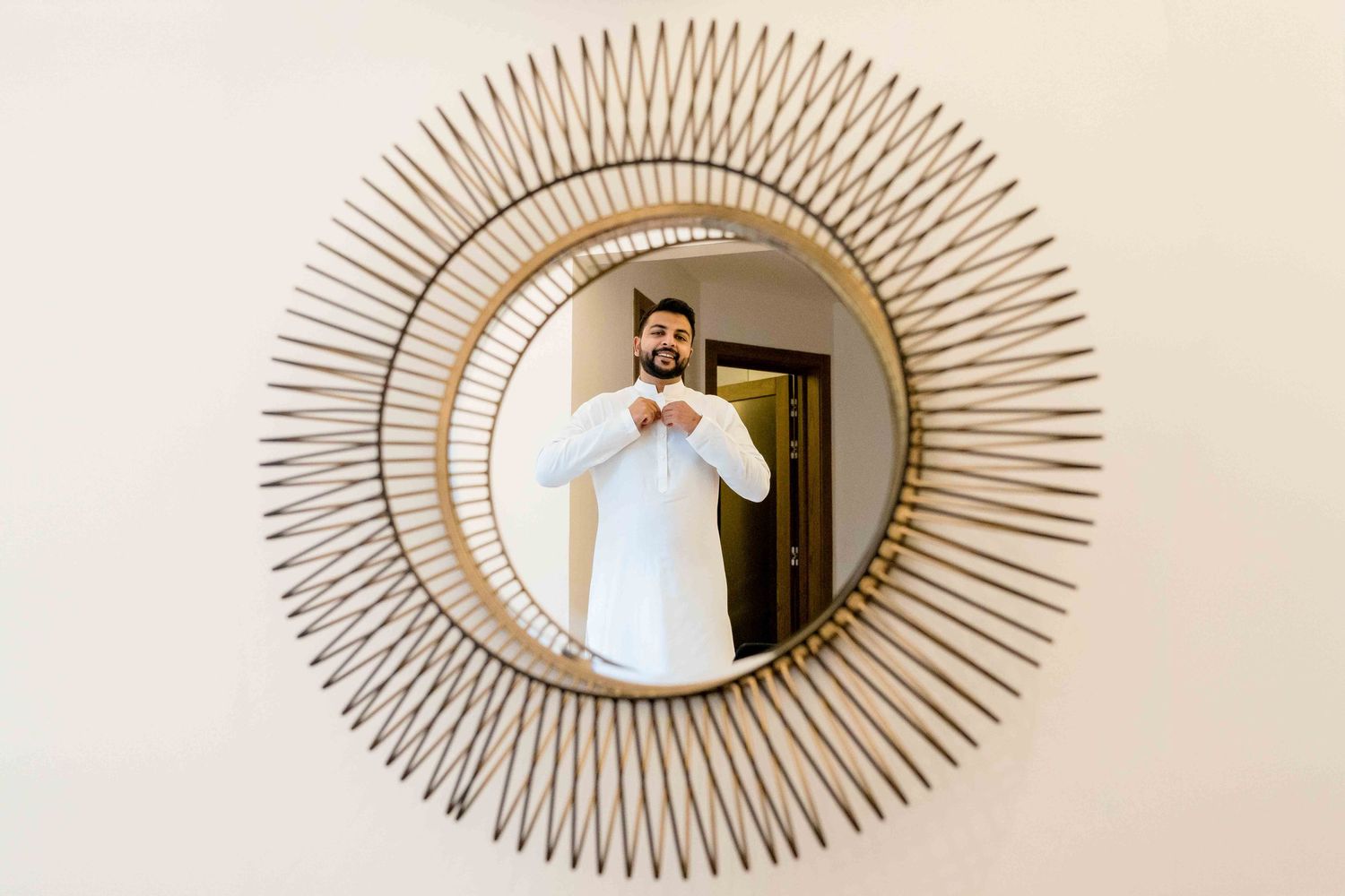 Decorative sunburst mirror frame on white wall capturing a reflection during wedding preparations.