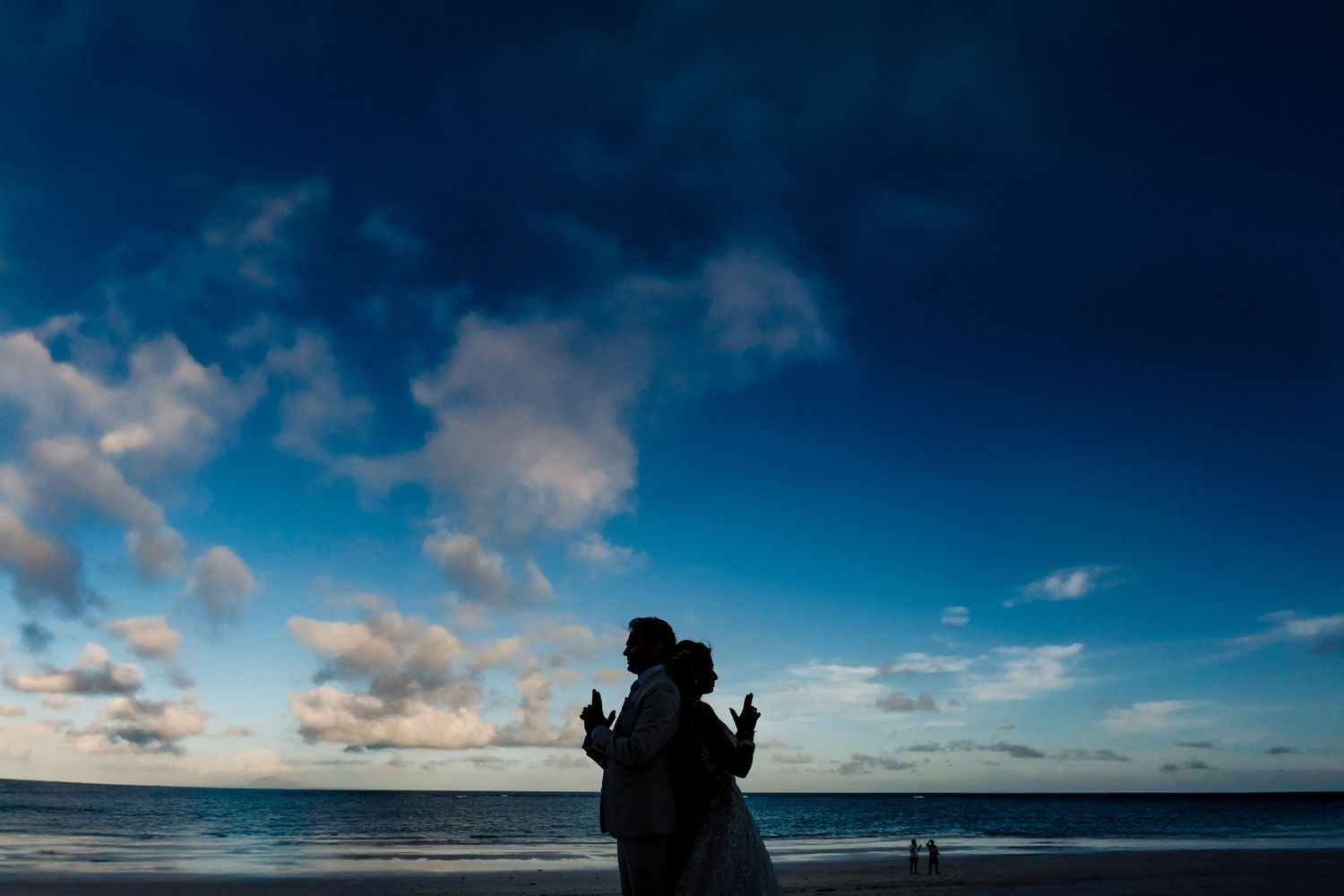 Silhouette of couple against blue sky and clouds at beach during sunset.