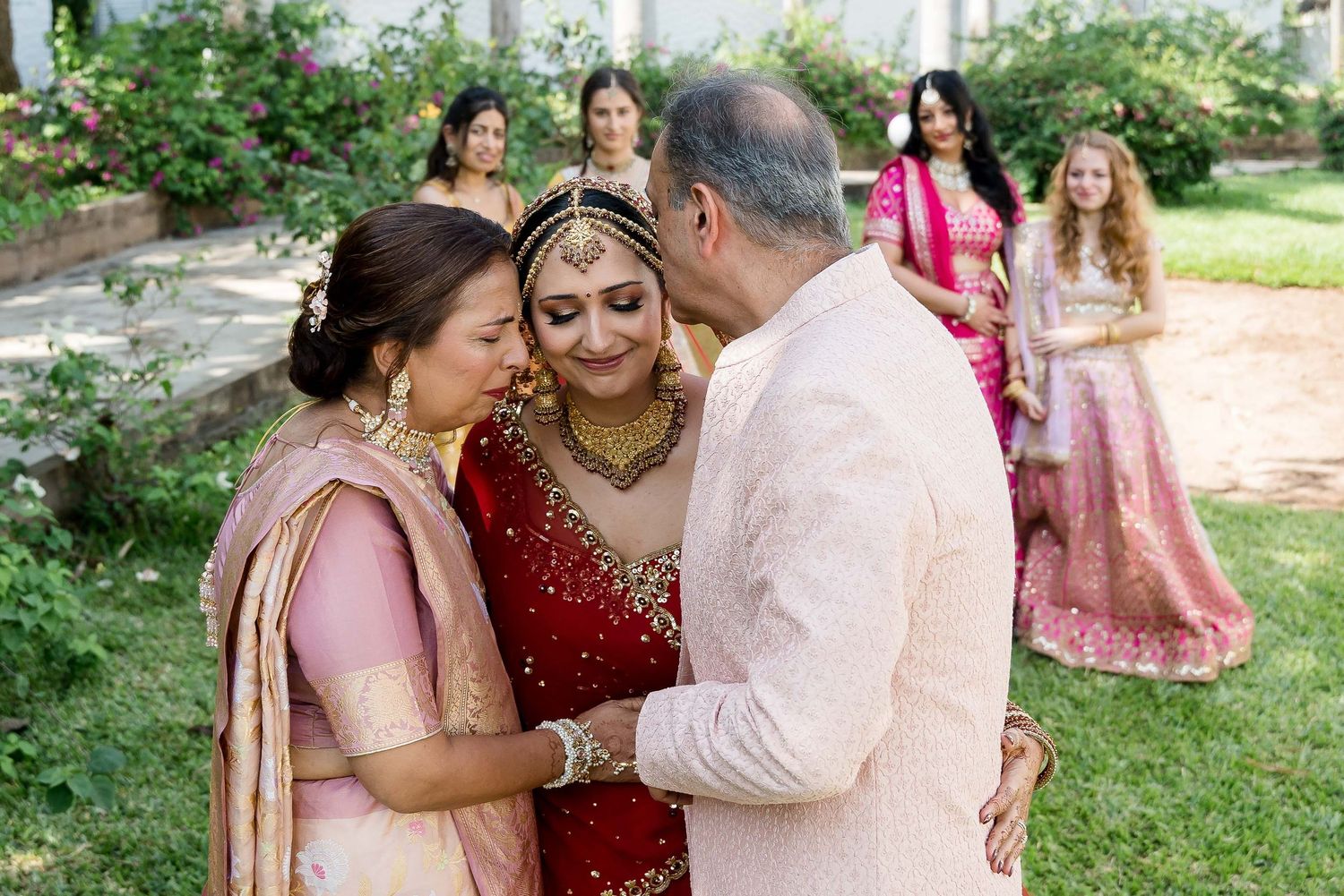 Couple embraces during an outdoor Indian wedding ceremony while guests look on in traditional attire.