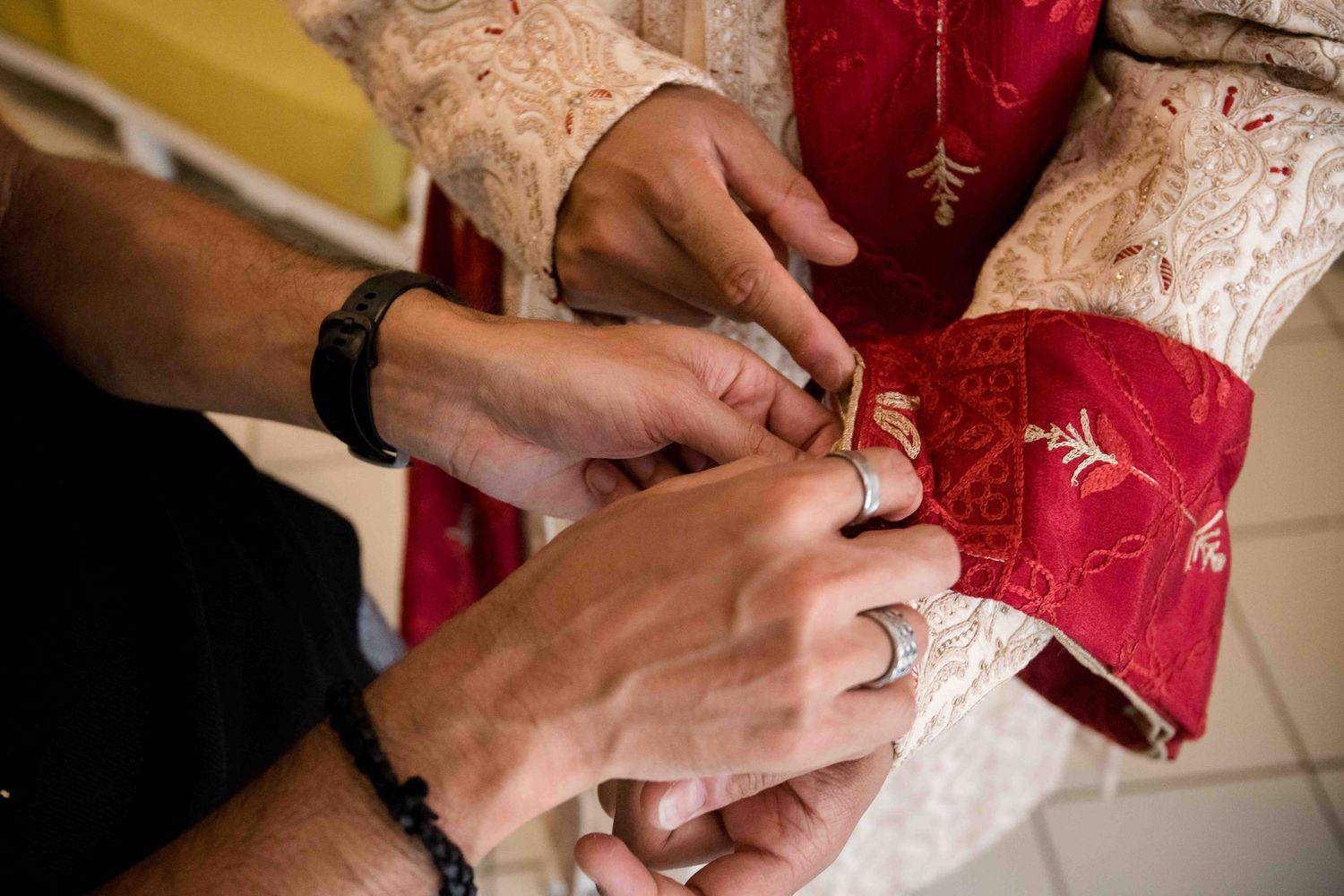 Hands fasten traditional red and gold Chinese wedding attire with delicate embroidered details.
