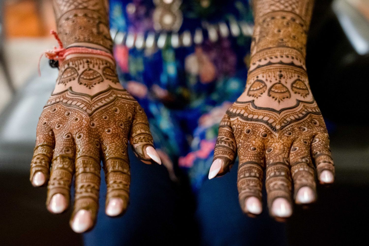 Detailed traditional henna mehndi designs adorning both palms against dark fabric.
