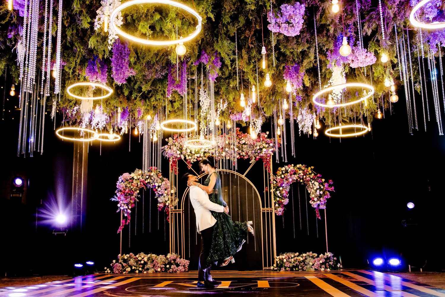 Elegant wedding reception venue with glowing golden halo chandeliers and purple uplighting creating a romantic atmosphere.